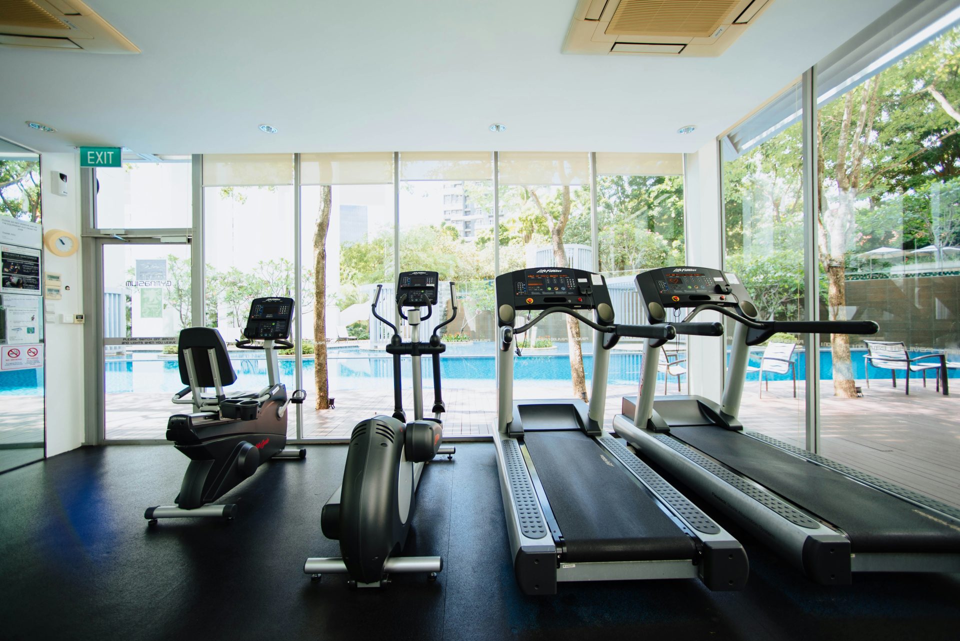 Fitnessgeräte in hellem Raum mit Blick auf Pool